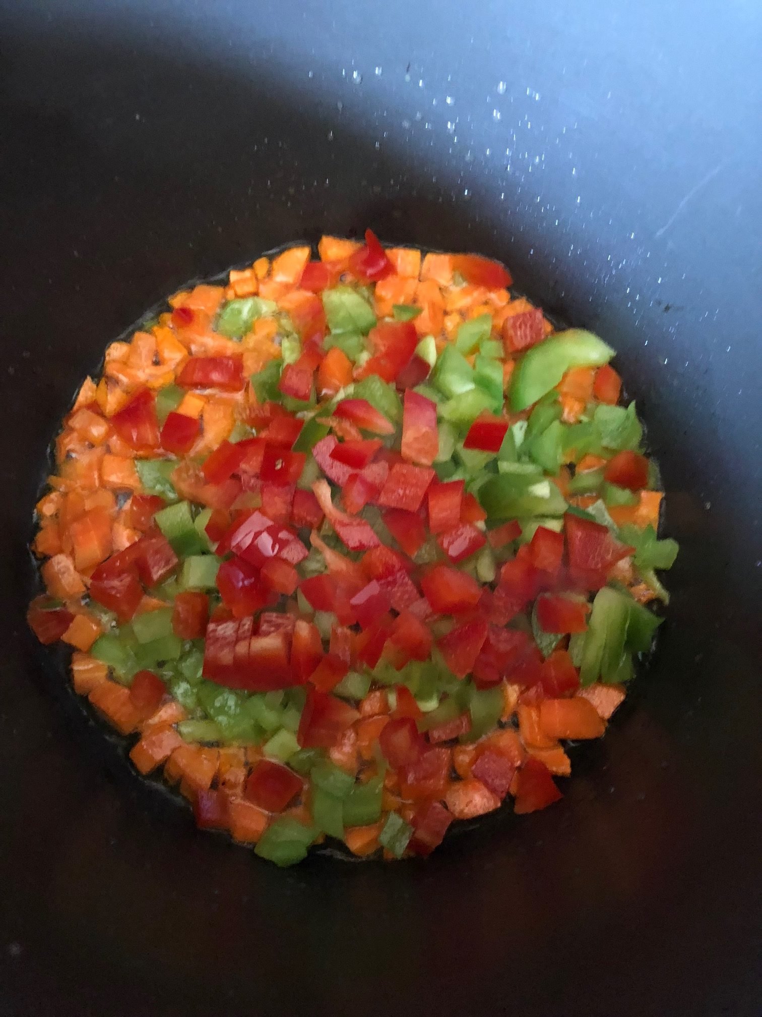 Chopped veggies being cooked with oil in a black non stick pot