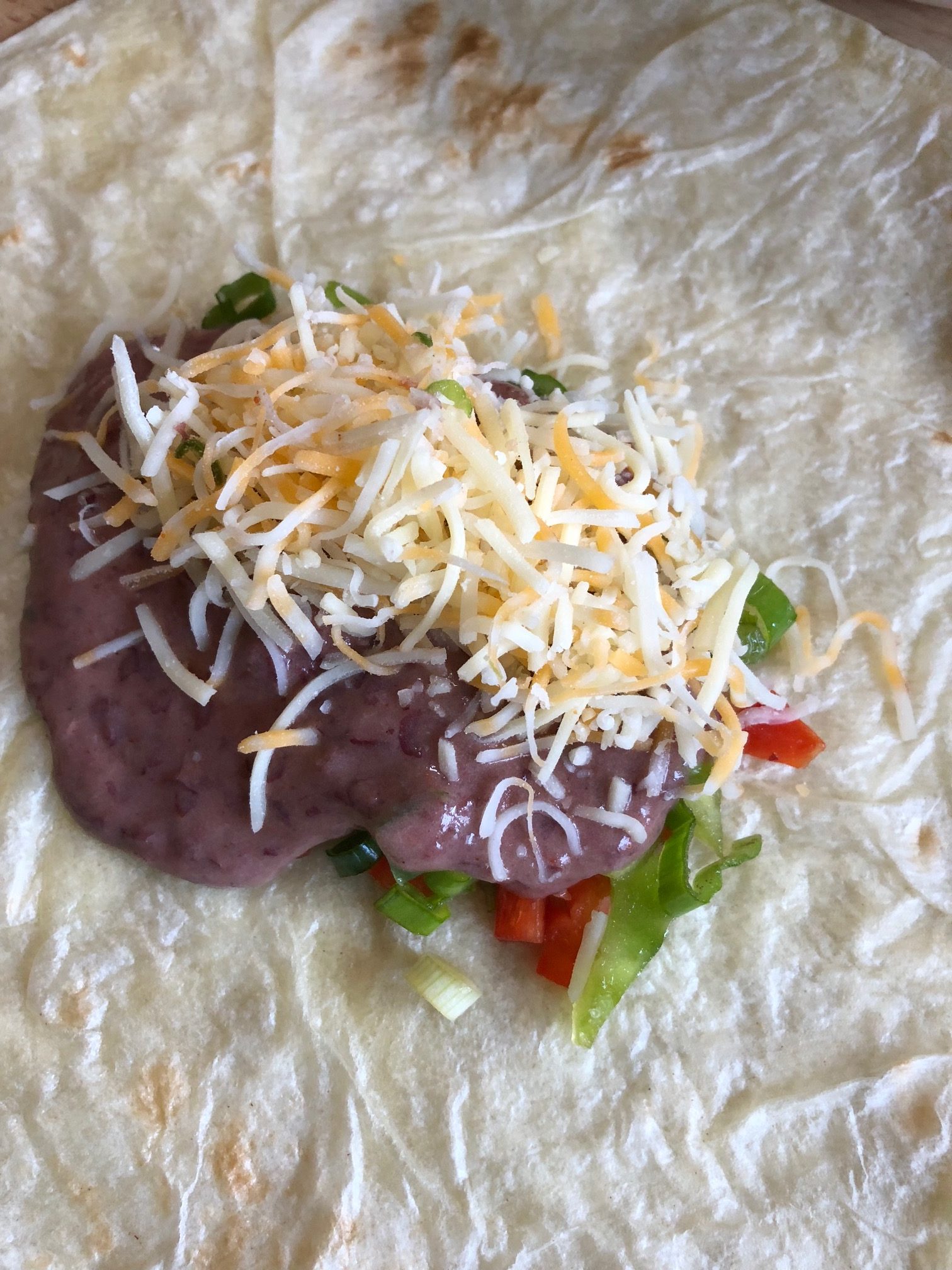tortilla with ingredients inside. The ingredients include refried beans, vegetables, and shredded cheese.