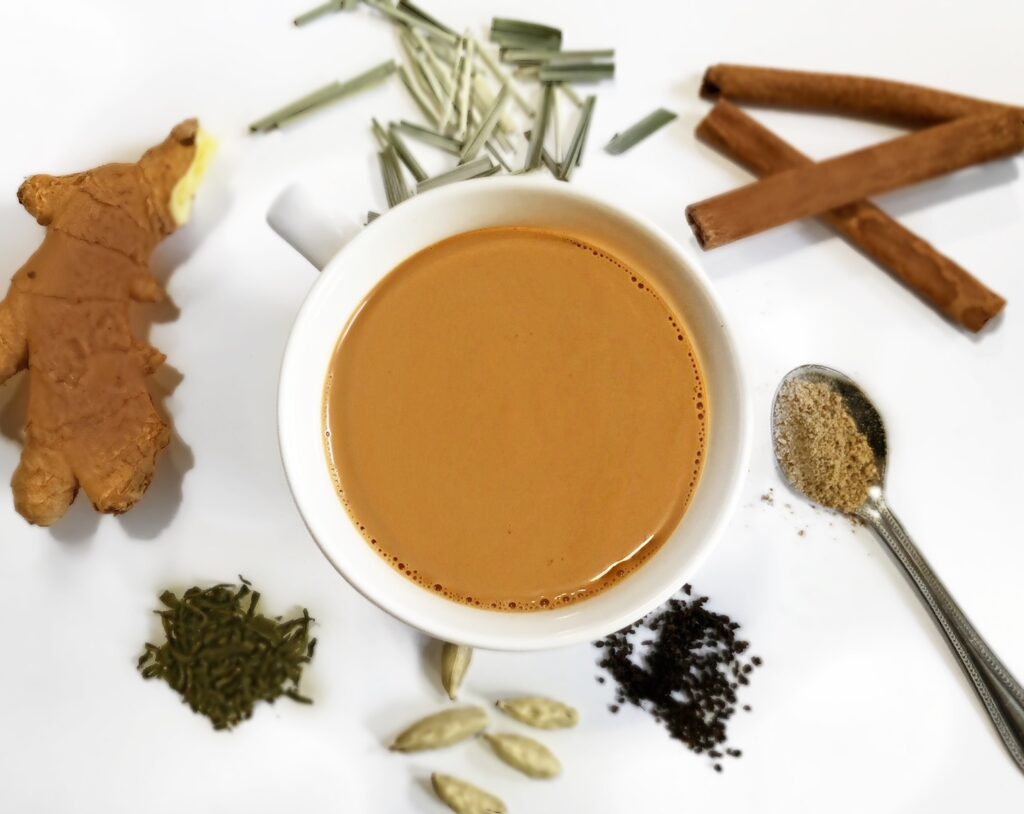 an authentic cup of chai or milk tea surrounded by spices and ginger root.