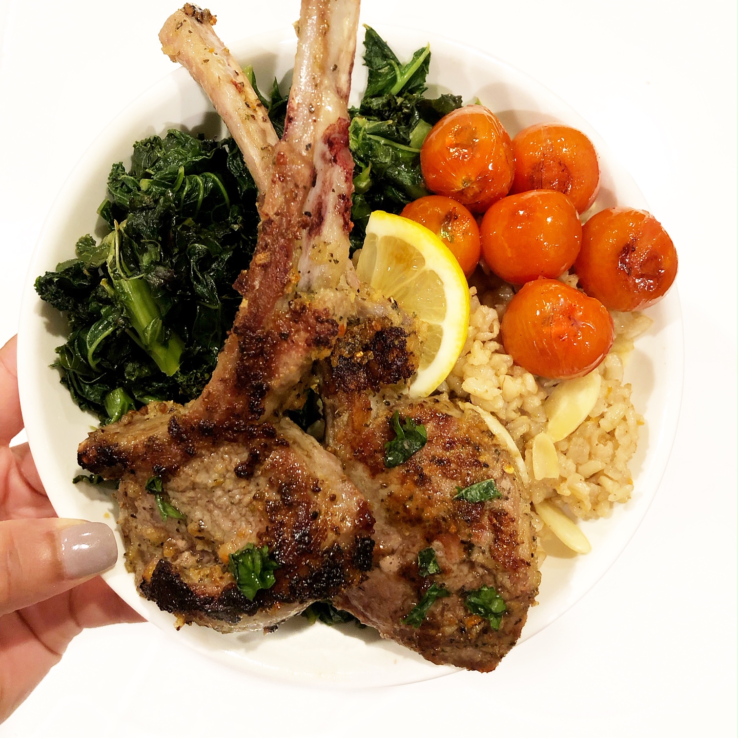 cooked lamb chops with roasted tomatoes, salad, and masala rice in a plate held by a hand with purple nail polish