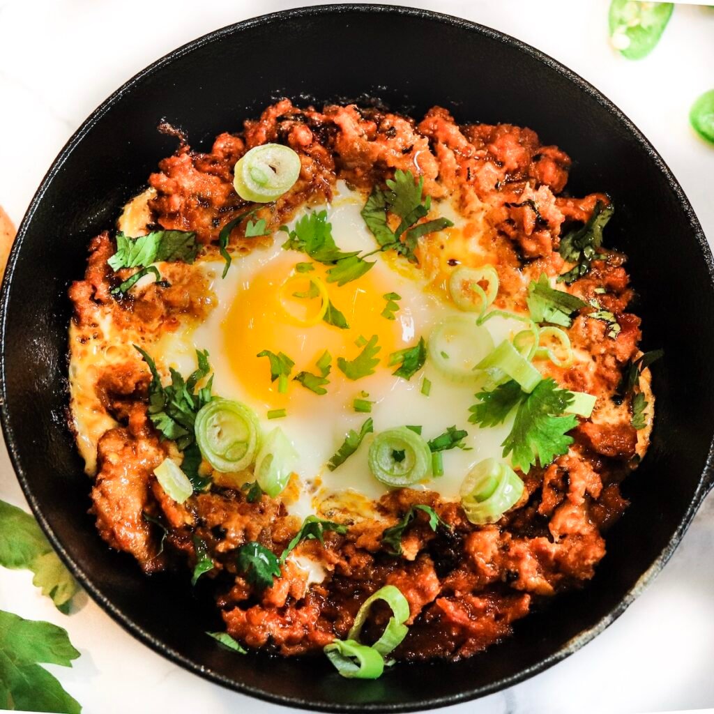 shakshuka with meat chicken and eggs indian breakfast in a bowl with runny egg