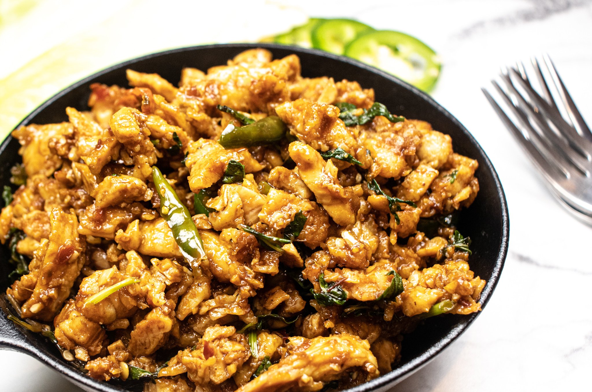 asian fusion minced meat chicken dish with thai basil in a cast iron pan that shows thai chillies on top