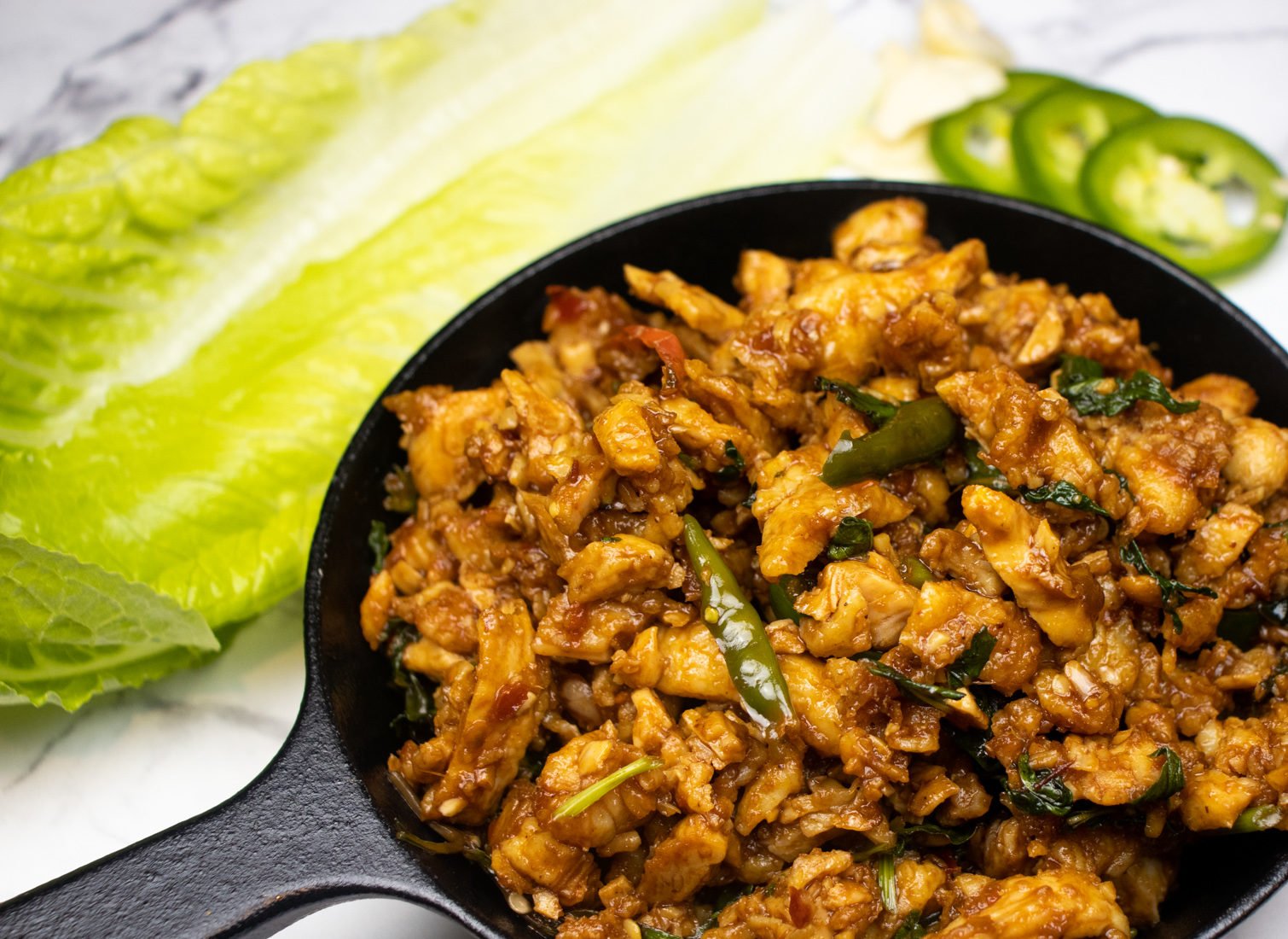 asian fusion minced meat chicken dish with thai basil in a cast iron pan and jalapenos on the side