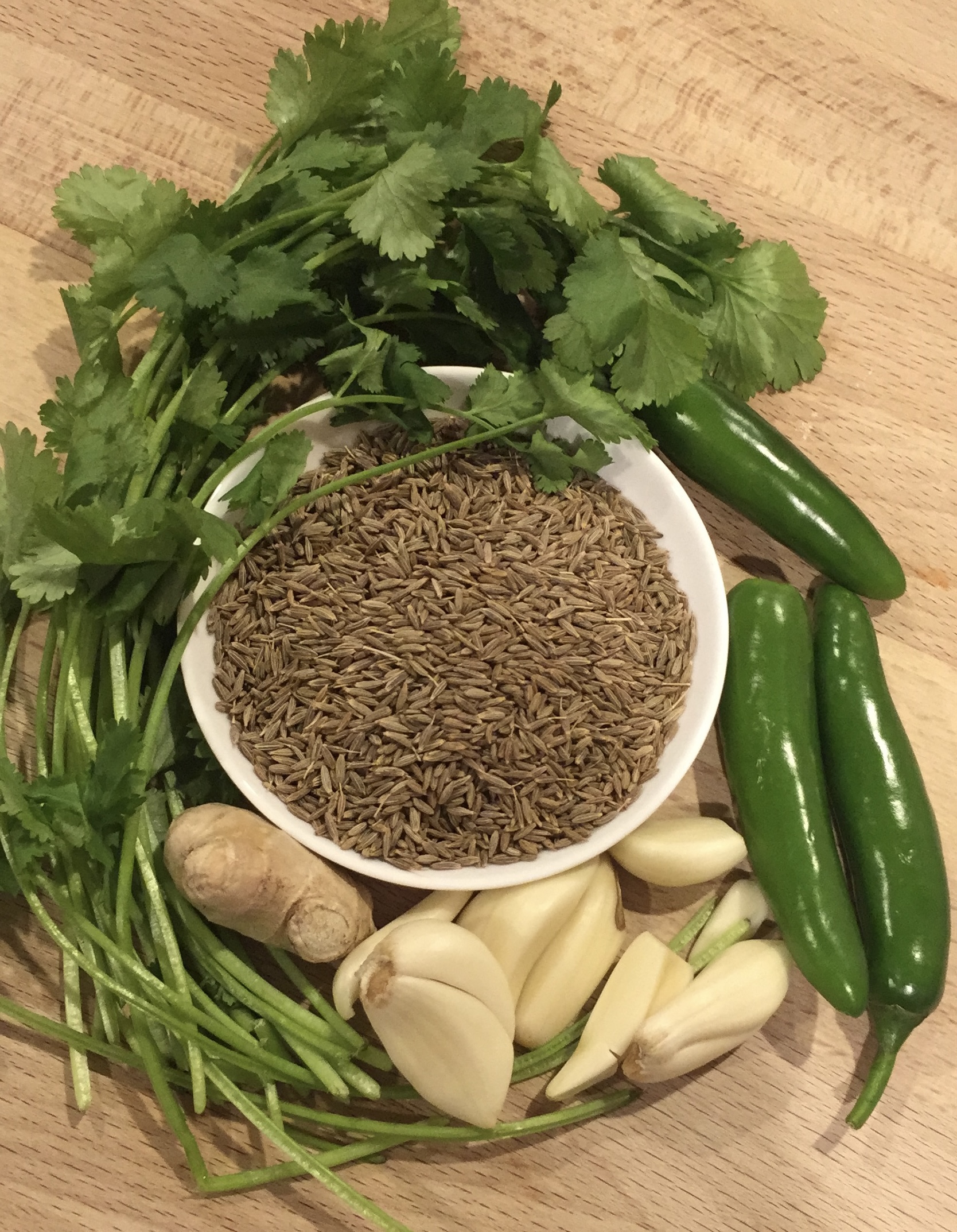 chutney ingredients for zhoug sauce. cilantro, cumin seeds, garlic, ginger, and chili peppers in a picture.