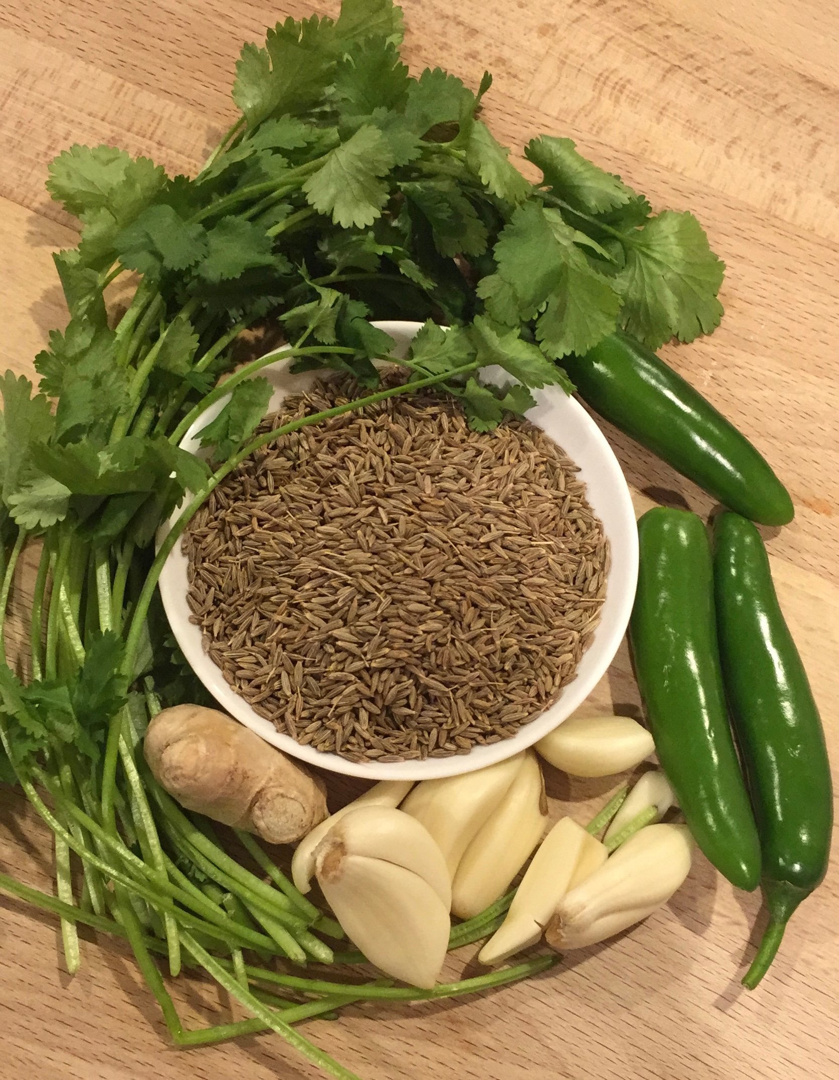 chutney ingredients for zhoug sauce. cilantro, cumin seeds, garlic, ginger, and chili peppers in a picture.