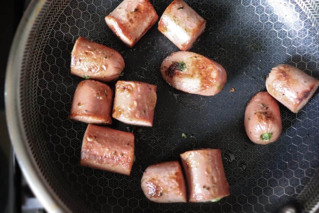 cooking chopped hot dogs with spices in a pan