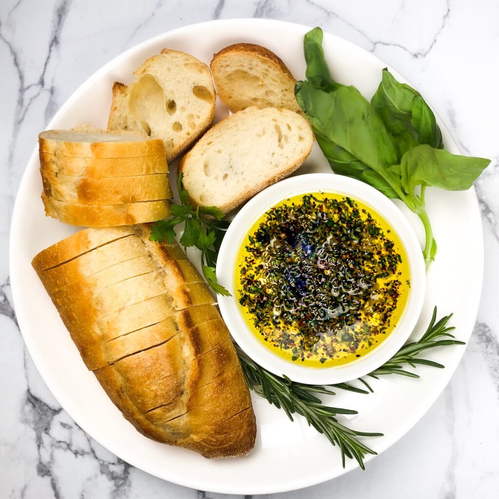 a round plate with bread and oil with fresh herbs that are dark green and bright red pepper flakes.