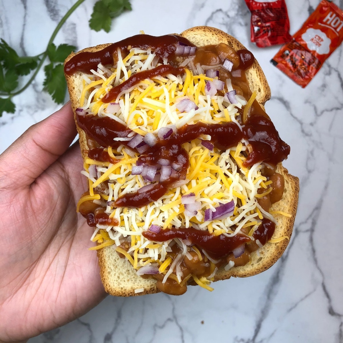 A sliced bread with a layer of baked beans, cheese,and hot sauce