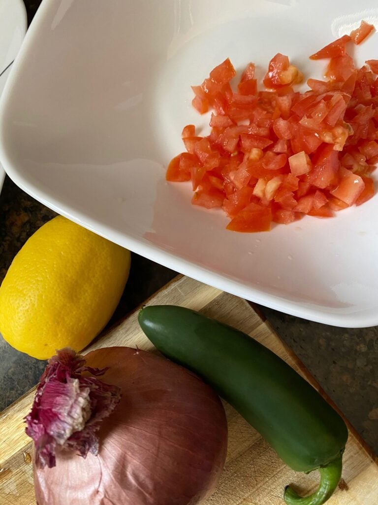 chopped tomatoes in a bowl with green jalapeno, onion, and lemon on the side.