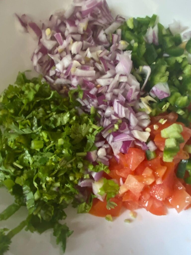herbs and vegetables in a bowl. cilantro, tomato, red onions, and jalapeno chopped finely. 