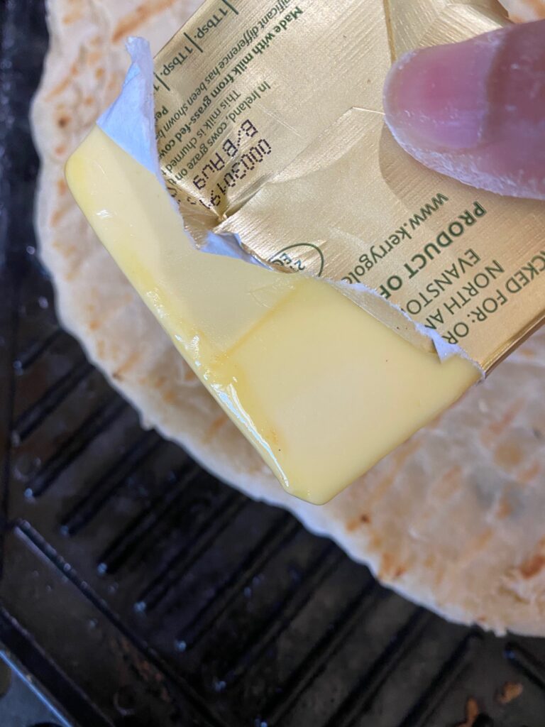 A stick of butter being used to slather on the edges of a pizza.