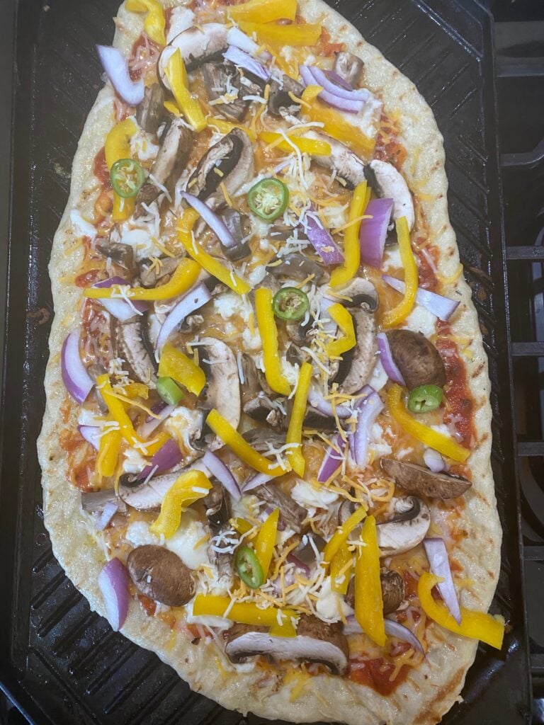 A pizza being grilled indoors on a stove top grill pan.