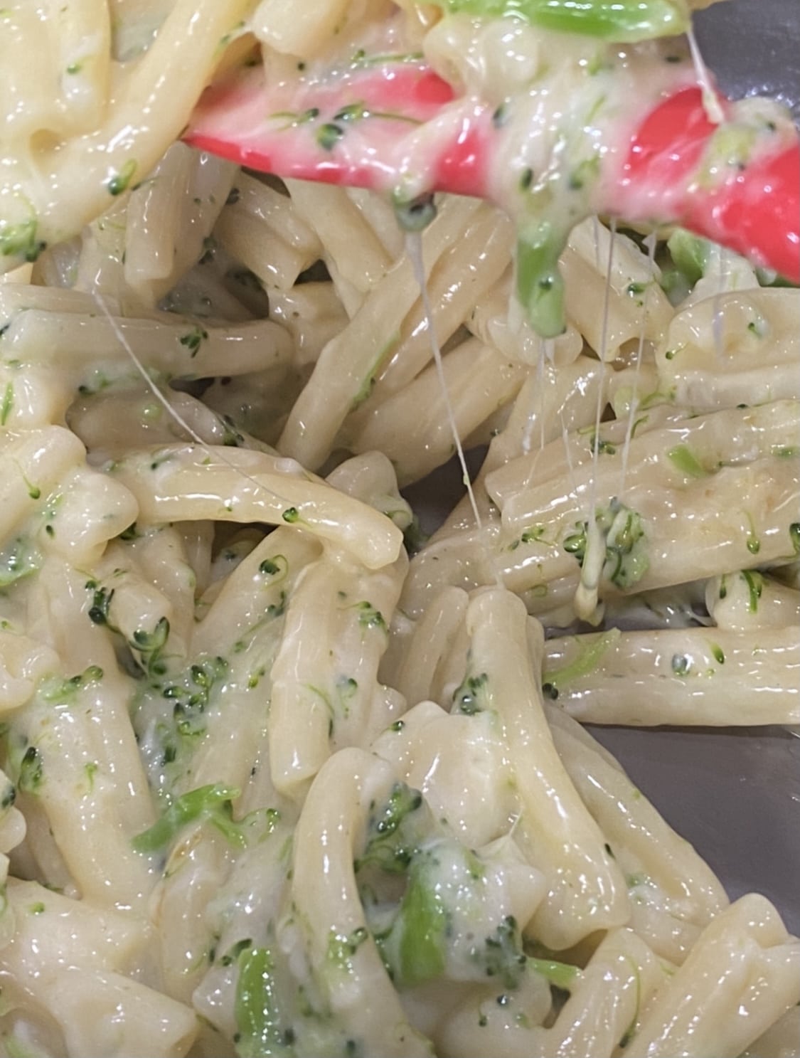 a red spatula holding a cheesy pasta withvegetables