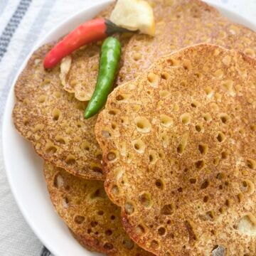 Savory rice pancakes with indian spices in a plate stacked and staggered with two thai peppers and lemon wedge