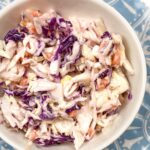 a blue plate topped with white bowl full of colorful healthy cole slaw