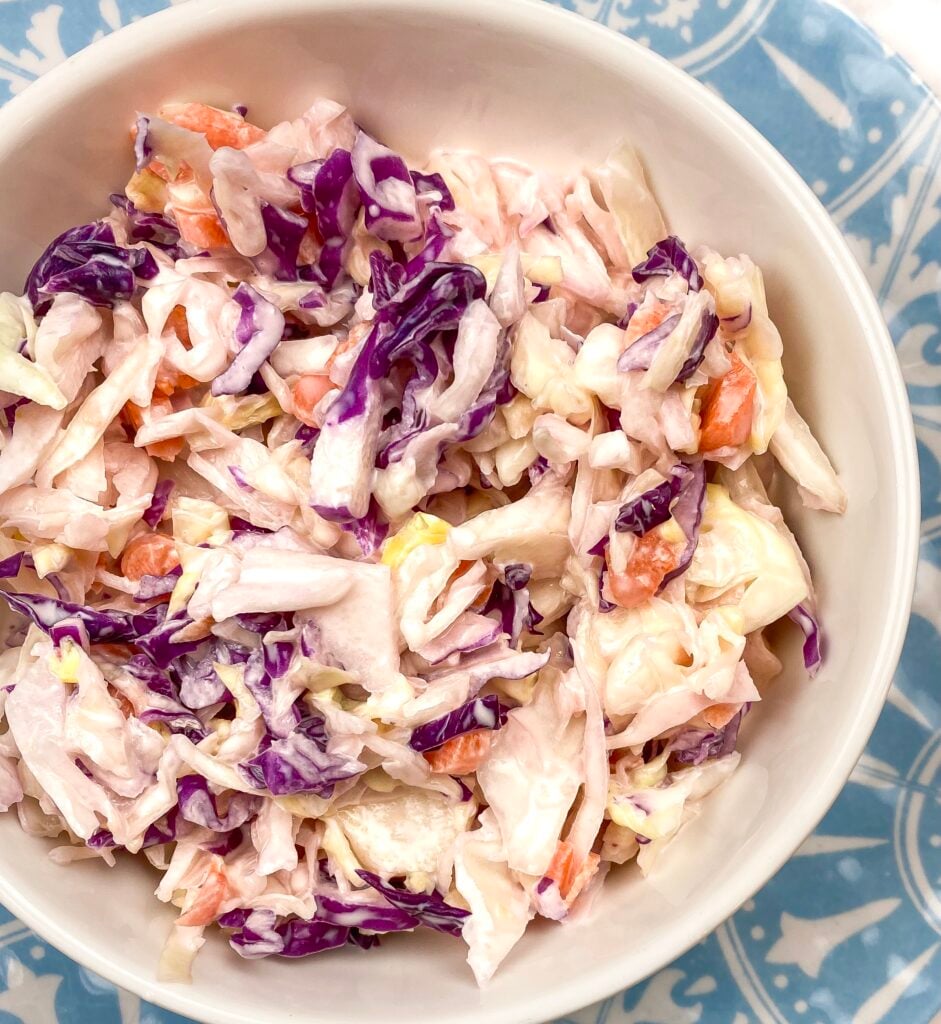 a blue plate topped with white bowl full of colorful healthy cole slaw