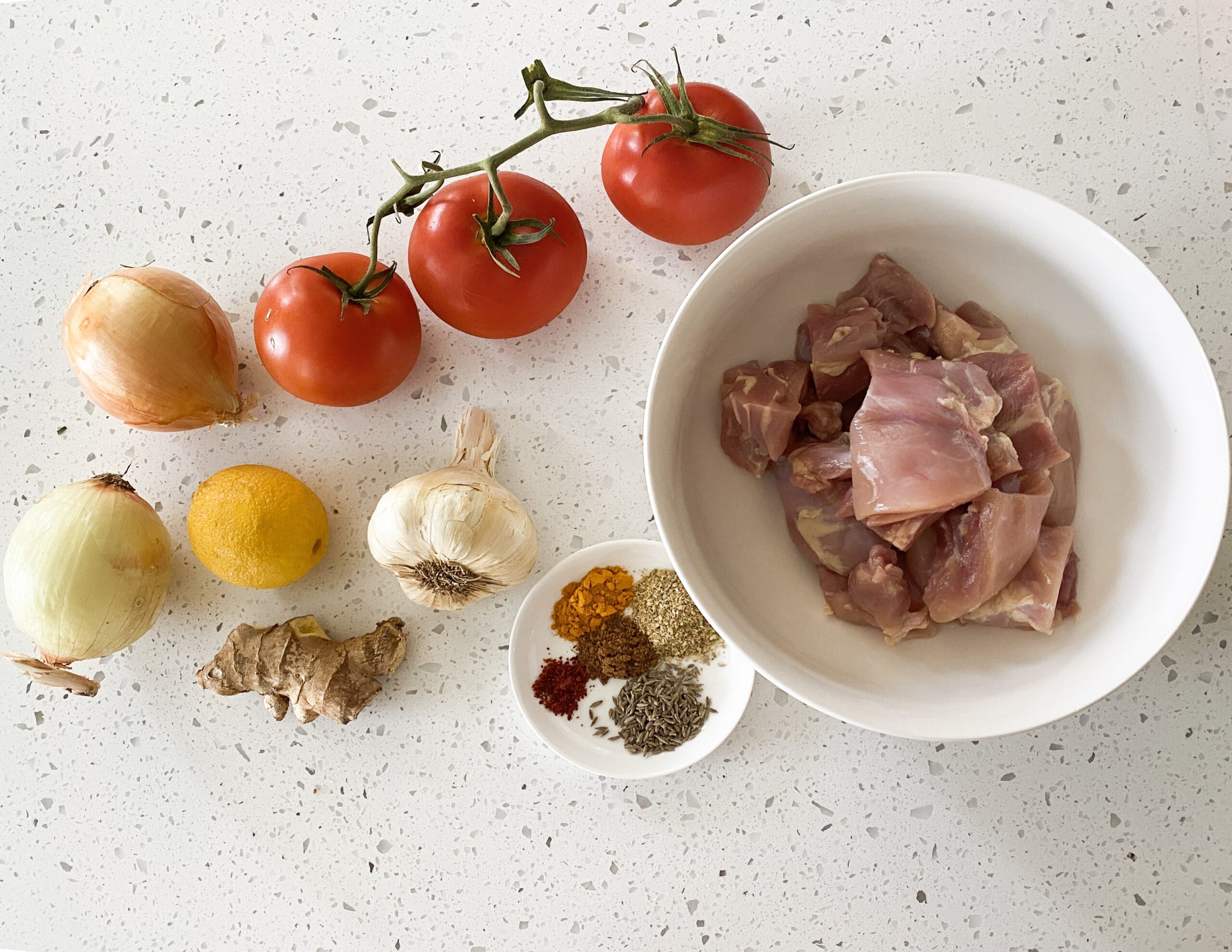 ingredients for desi chicken tapelu chicken on a counter tomatoes onions garlic ginger and raw chicken