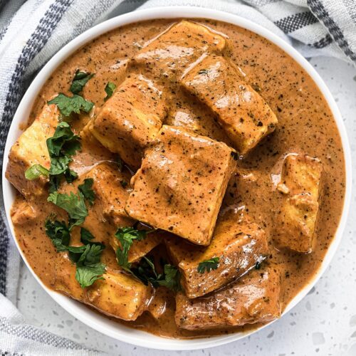 paneer butter masala in a round bowl with cilantro on the edge