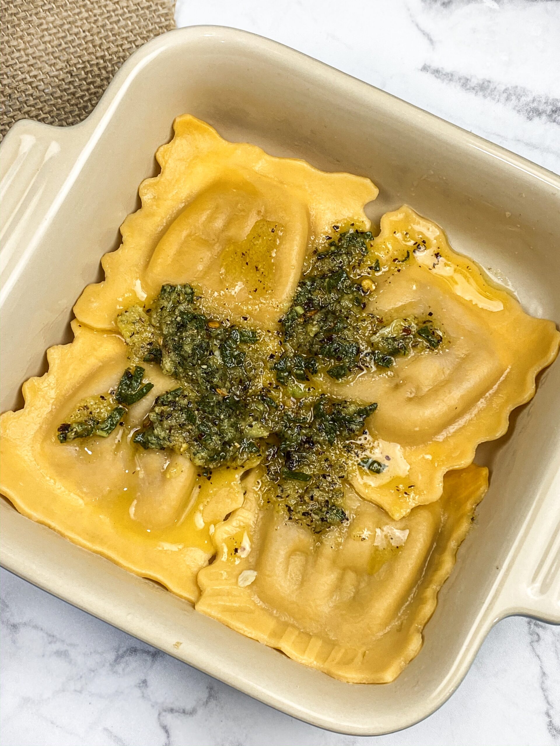 layering pasta in a le creuset pan with herbs on top