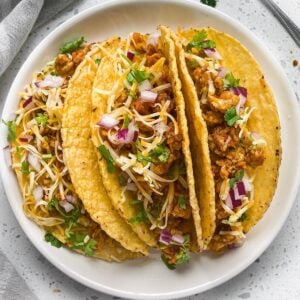 keema chicken tacos in hard shells three of them in a round plate with cilantro on top