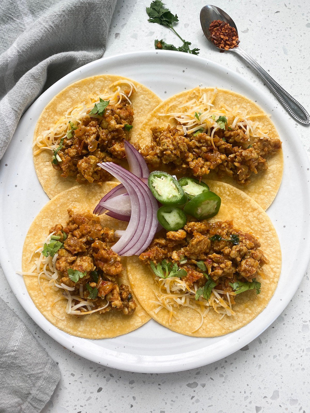 4 corn tortillas in a round plate with ground chicken and cheese lettuce onion and green peppers