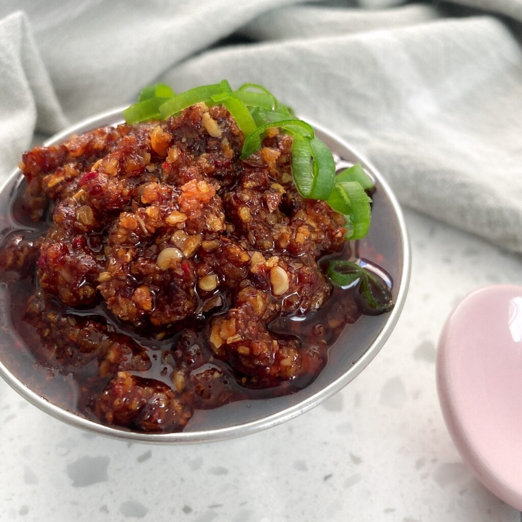 a small round bowl with spicy pepper chutney and green onions on top