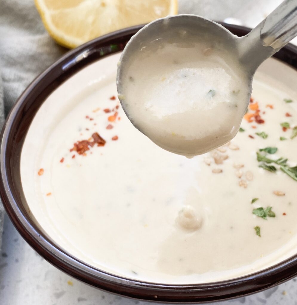 pouring lemon herb tahini sauce from ladle to show thick consistency