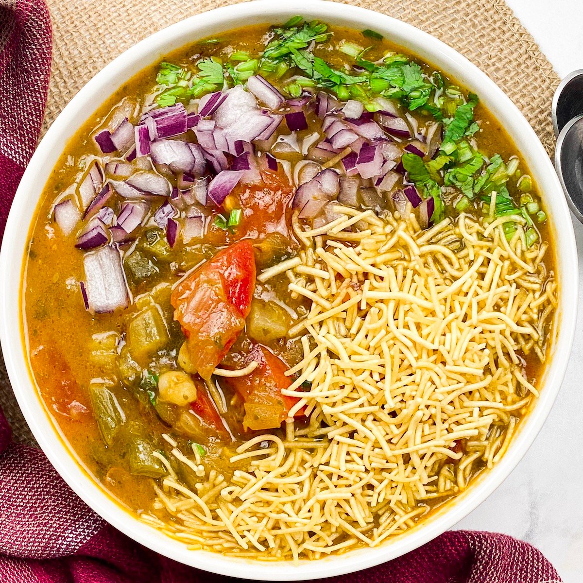 sev usal in a bowl with onions, tomatoes, cilantro, and soup